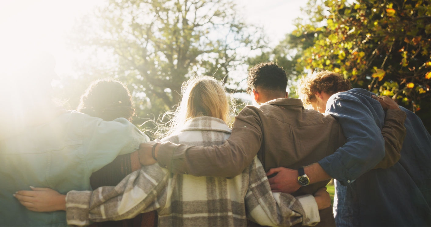 Group, back and friends to relax outdoor on school break, discussion and hug for bonding in summer. People, students and embrace with , care and trust together for social reunion at park
