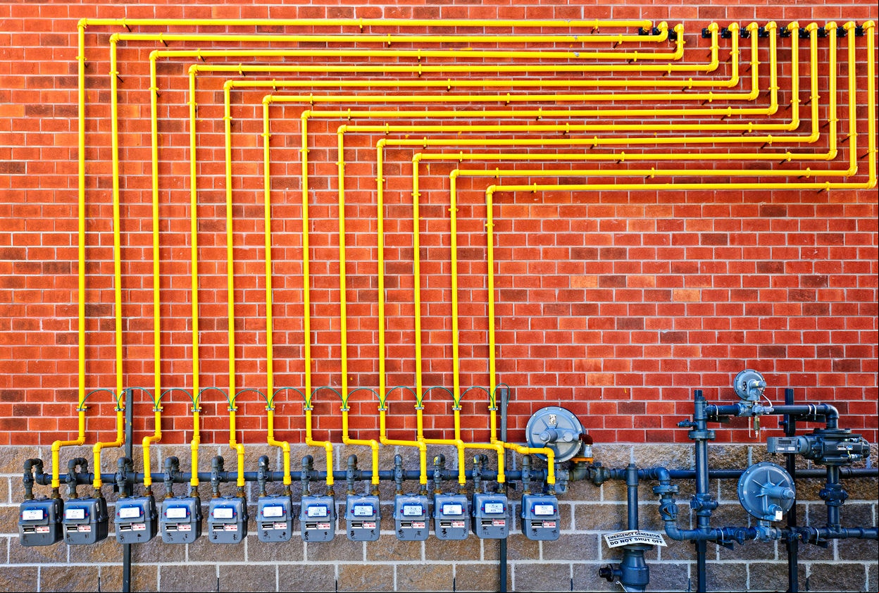 Row of natural gas meters with yellow pipes on building brick wall