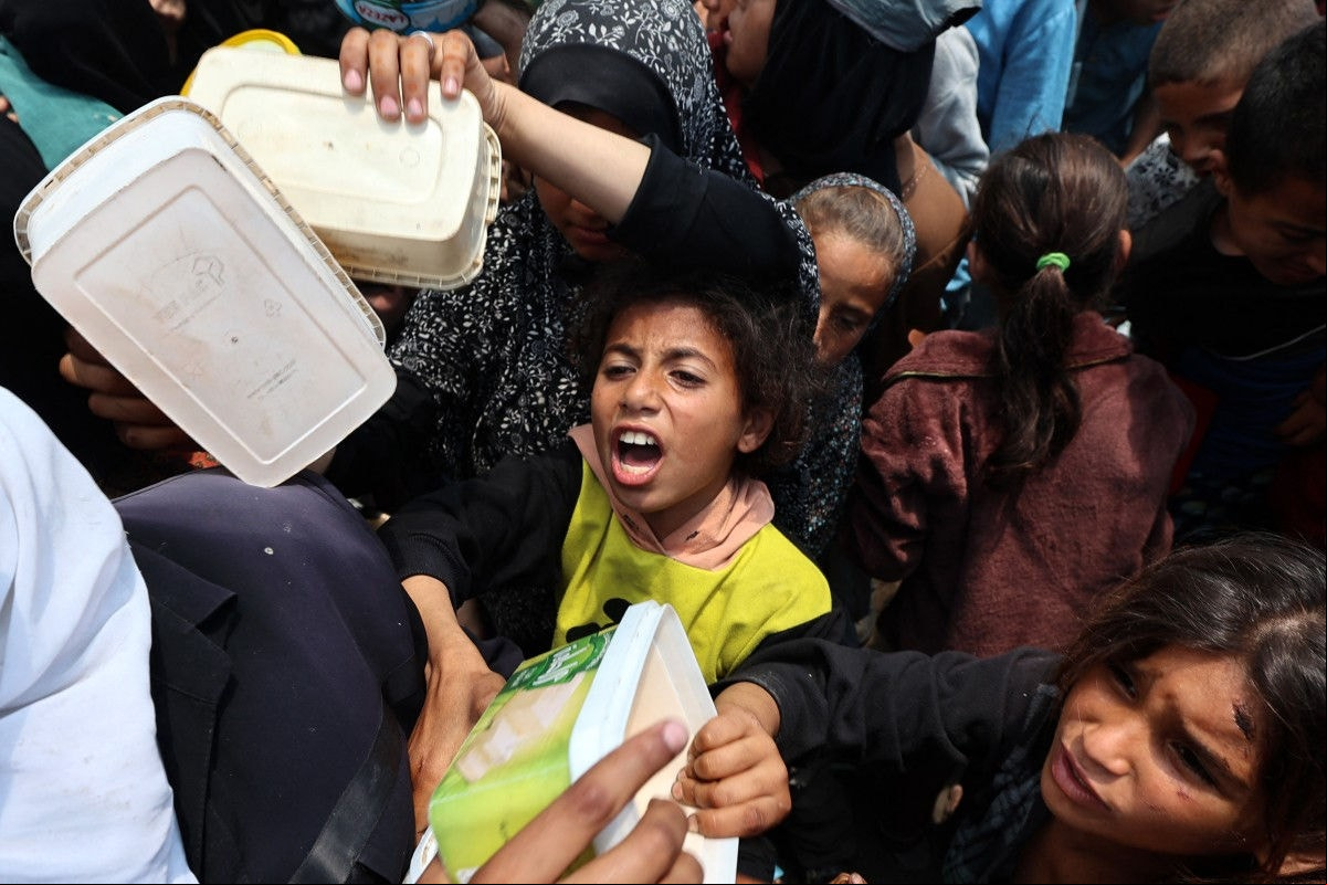 Uma menina palestina reage quando as pessoas se reúnem para uma refeição quente em um ponto de distribuição de alimentos no campo de Nuseirat para refugiados no centro da Faixa de Gaza, onde moradores esperam desesperadamente por suprimentos vitais em 21 de maio, depois que Israel disse que deixou entrar dezenas de caminhões da ONU